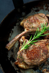 Grilled lamb chops with rosemary against a dark background.