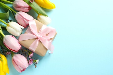 Beautiful tulips with gift box on colored background