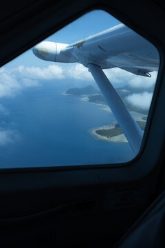 Aerial view through aircraft side window flying over tropical waters.