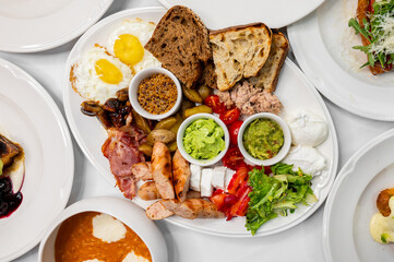 A vibrant breakfast platter featuring eggs, toast, smoked salmon, olives, guacamole, tomatoes, bacon, and fresh greens. Perfect for a hearty start to the day.