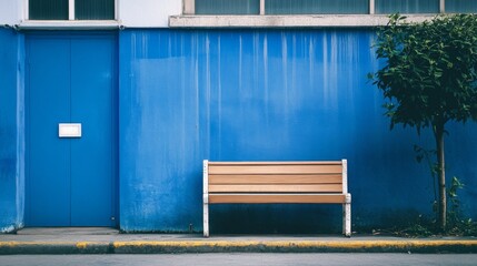 Wooden bench against a blue wall beside a door and small tree.