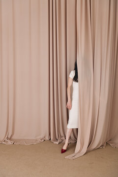 Mysterious Woman Half-Hidden Behind Elegant Beige Curtain