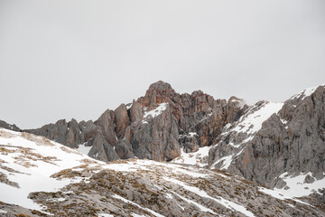 Snow-dusted rocky peaks of Pe&ntilde;a Vieja dominate the landscape in Picos de Europa, showcasing the stark beauty of the mountains during winter. A dramatic display of nature's raw power and elegance.