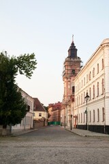 Naklejka premium Ancient buildings and a historic chapel on a city street on a sunny day. An architectural ensemble with elements of baroque and classicism, surrounded by greenery.