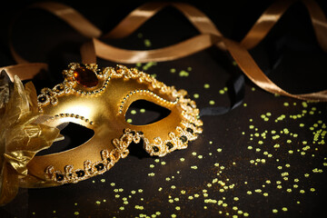 Beautiful carnival mask, ribbon and confetti on dark background, closeup