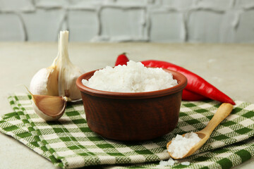 Sea salt in bowl, garlic and chili peppers on grey table, closeup