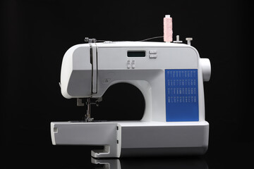 One sewing machine with spool of thread on black background