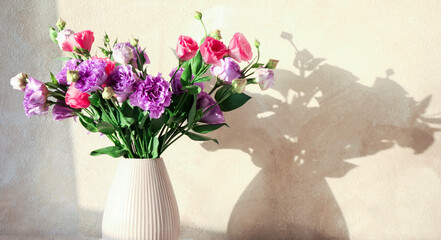 Vase with beautiful eustoma flowers near beige wall, closeup. Space for text