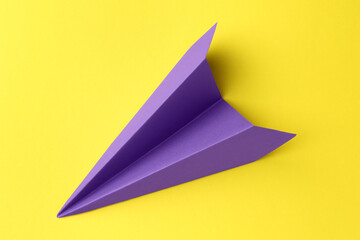 One handmade purple paper plane on yellow background, top view