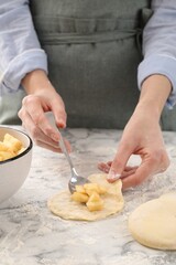 Woman making pirozhki (stuffed pastry pies) with apples at white marble table, closeup