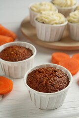 Tasty carrot muffins with cream and fresh vegetable on white wooden table, closeup
