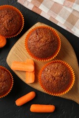 Tasty carrot muffins with fresh vegetables on black table, flat lay