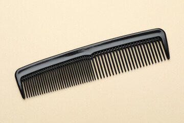 One black plastic comb on beige background, top view