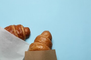Paper bags with fresh croissants on light blue background, top view. Space for text