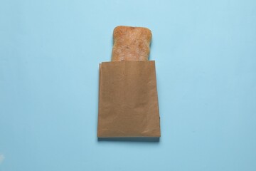 Paper bag with fresh ciabatta on light blue background, top view