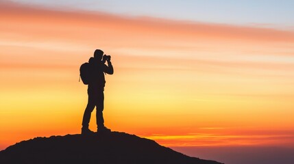 Obraz premium A silhouette of a person with a camera against a vibrant sunset, capturing the beauty of nature from a mountain peak.