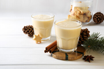 Tasty Christmas cocktail (eggnog) in glasses, pine cones and spices on white wooden table