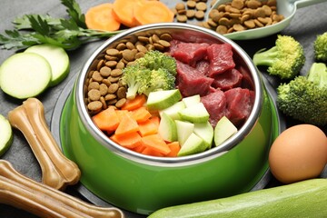 Natural and dry pet food in feeding bowl among products on dark table, closeup