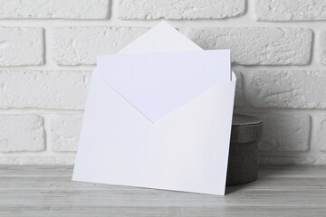 Paper envelope with letter on wooden table near white brick wall. Mockup for design