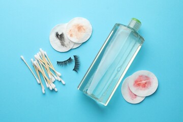 Dirty cotton pads, swabs, bottle of makeup remover and false eyelashes on light blue background, flat lay