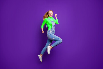 Full size photo of cheerful girl raising her fists screaming yeah wearing yellow turtleneck denim jeans isolated over purple violet background