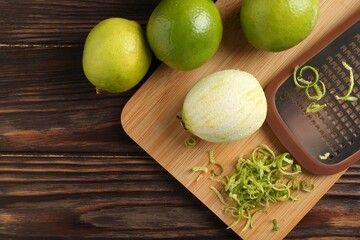 Lime zest, grater and fresh fruits on wooden table, flat lay. Space for text