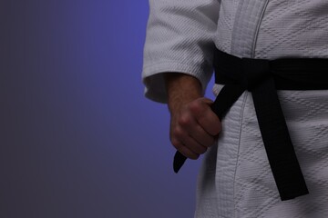 Karate fighter in uniform on dark purple background, closeup. Space for text