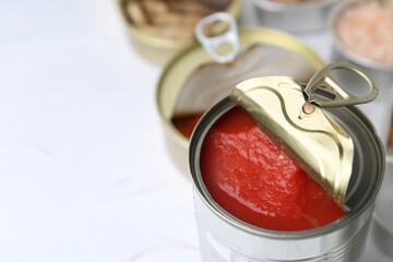 Open tin cans with different preserved products on white table, closeup. Space for text