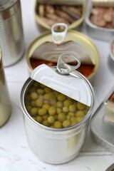 Open tin cans with different preserved products on white table, closeup