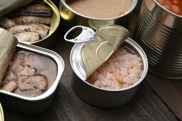 Open tin cans with different preserved products on wooden table, closeup