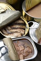 Open tin cans with different preserved products on table, closeup