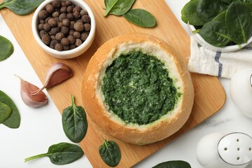Delicious spinach sauce in bread bowl on white table, flat lay