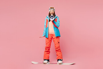 Full body young amazed woman in warm blue padded jacket ski goggles mask spend weekend winter...