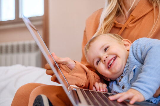 Smiling child lay down on laptop while mom works