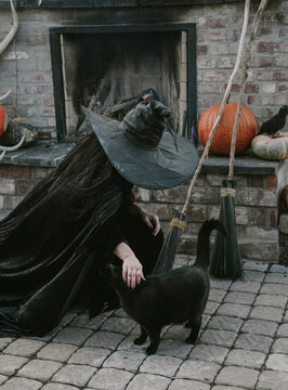 witch leans own to pet her black cat near outside fireplace