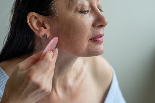 Mature beautiful woman gives herself a gua sha massage on her face