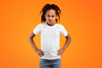 People Emotions, Anger Concept. Portrait of stubborn young African American girl posing with hands on hips, standing isolated on yellow studio wall. Angry displeased kid looking at camera