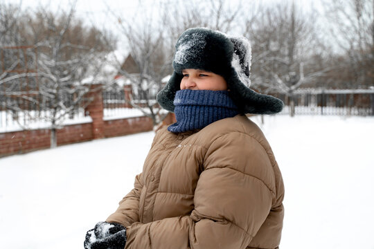 Happy boy playing snowball fight during snowfall in winter outdoors.