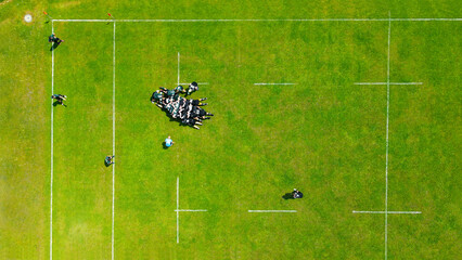 Aerial View of Rugby Scrum on Green Field. A top-down aerial view of a rugby match in progress, highlighting a scrum formation on a vibrant green field with white markings.