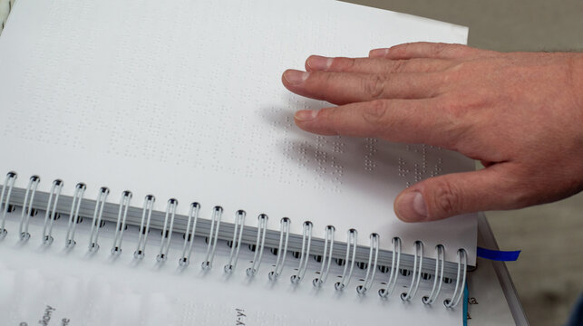 Male fingers reading a book page with braille
