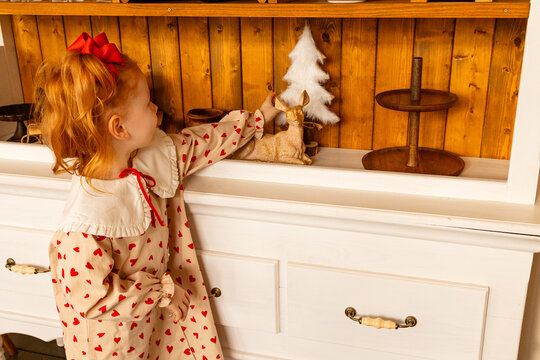 Little girl decorates a shelf with festive items in a cozy room