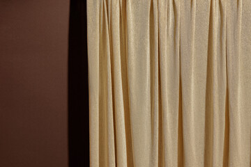 Gold curtain fully covering a dark brown wall surface