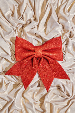 Large red glitter bow on shiny cream fabric background