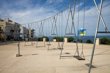Fototapeta premium Swing on a metal chain on an empty embankment. Center of the Polignano a Mare village, in province of Bari.