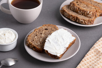 Slices of whole grain bread topped with cream cheese on a plate in a cozy kitchen setting