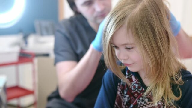 Portrait of cute little girl during appointment of dermatologist in modern clinic. Doctor examines child hair and scalp for lice and nits. Pediculosis and parasitic diseases are common in kids groups