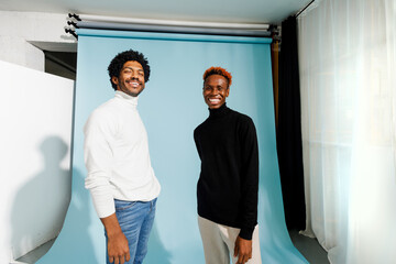 Two smiling young men pose in a modern studio 