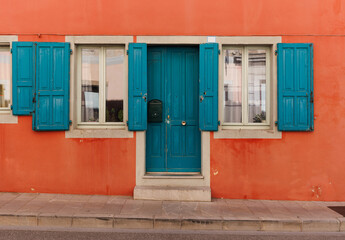 Orange Italian house facade in a typical town of Italy with green doors and windows