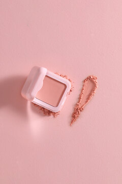 An open makeup compact with powder design on a pink textured bac