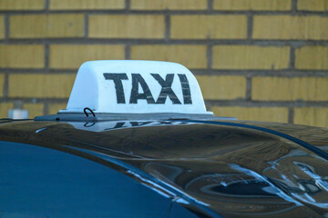 A taxi is parked with a white rooftop sign displaying the word 'TAXI'. The vehicle is positioned in...